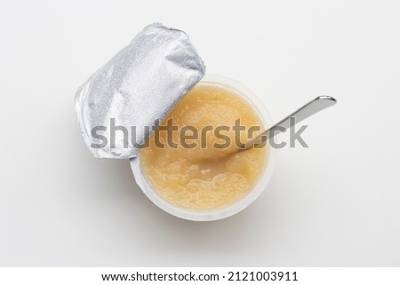 Top view of an opened cup of unsweetened applesauce with a spoon in it, isolated on a white background. Gluten-free vegan kids snack. Royalty-Free Stock Photo #2121003911