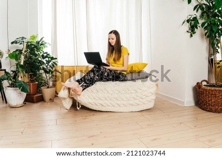 Smiling woman using laptop at home in bedroom.