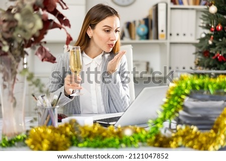 Female manager with a glass of champagne congratulates Merry Christmas on the Internet in the office