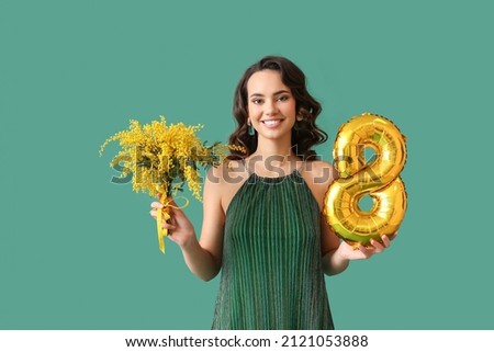 Smiling young woman with mimosa flowers and balloon in shape of figure 8 on green background. International Women's Day