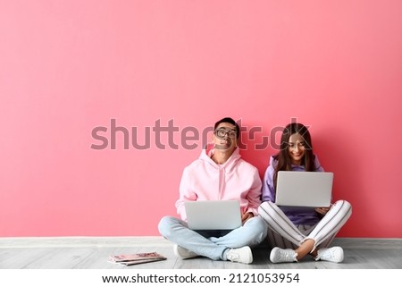 Young couple using laptops near pink wall