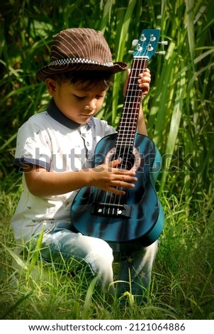 a cute asian boy playing guitar in the meadow