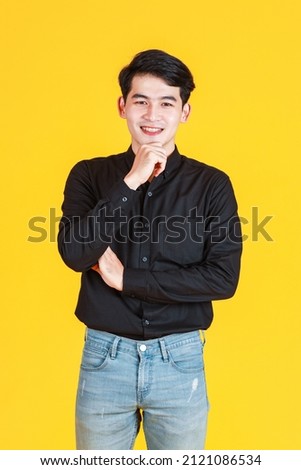Portrait studio shot of millennial Asian thoughtful doubtful professional successful male businessman in casual shirt and jeans outfit standing holding finger pointing forehead on yellow background.