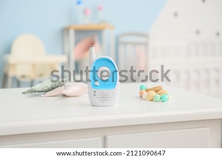 Modern baby monitor, toys and teether on table in room Royalty-Free Stock Photo #2121090647