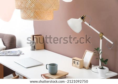 Modern workplace with laptop and lamps near color wall