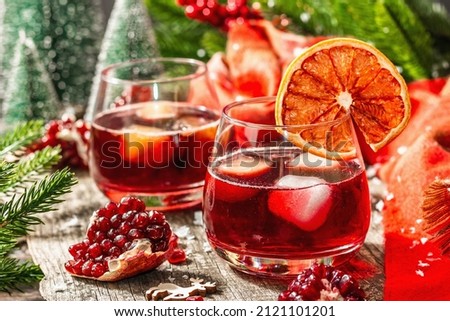 Non-alcoholic cocktail with fruits syrup and ice. Christmas traditional decor, New Year festive arrangement. Cozy scarf, evergreen branches, wooden background