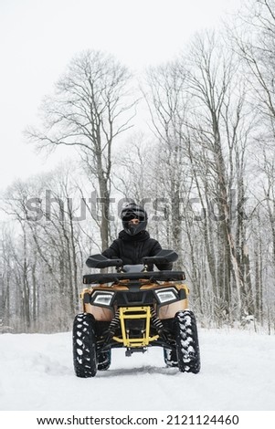 Hero shot of a man on a quad bike in winter background. Portrait of a quadricycle rider in snowy forest