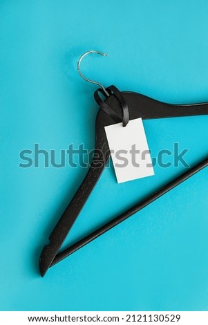 Clothes tag, empty label mockup template for your design. Empty ethics on a black wooden hanger on a light blue background. Promotion banner for clothing boutique