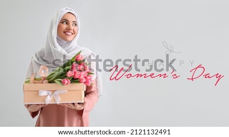 Beautiful greeting card for International Women's Day celebration with young Muslim woman holding gift Royalty-Free Stock Photo #2121132491