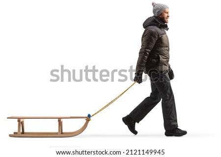Full length profile shot of a man in winter clothes walking and pulling a sled isolated on white background