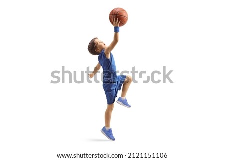 Full length profile shot of a boy in a blue jersey jumping with a basketball isolated on white background Royalty-Free Stock Photo #2121151106