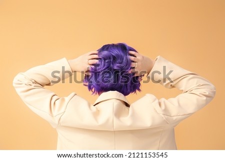Beautiful young woman with violet hair on color background, back view. Very Peri - color of year 2022