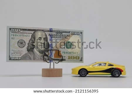 A toy car stands next to a banknote on a stand. Accurate financial calculation when buying a car