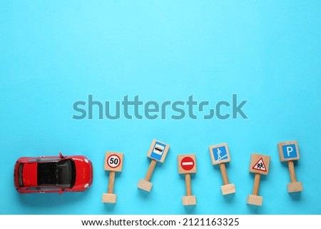 Many different miniature road signs and car on light blue background, flat lay with space for text. Driving school
