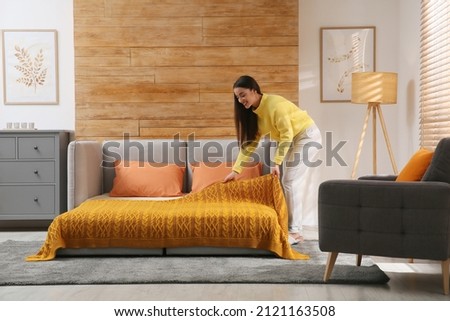 Young woman making bed in room. Modern interior with sleeper sofa Royalty-Free Stock Photo #2121163508