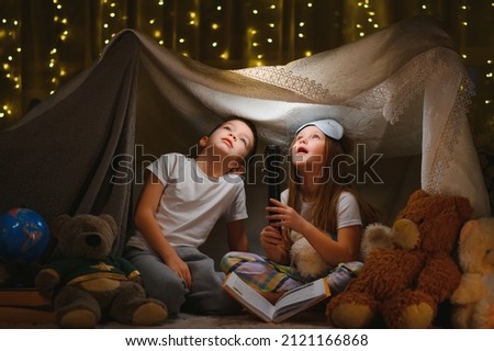 Two little child play at home in the evening to build a camping tent to read books with a flashlight and sleep inside. Concept of: game, magic, creativity, alarm systems Royalty-Free Stock Photo #2121166868