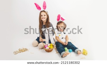 Happy children celebrate Easter. little girls wearing bunny ears enjoying egg hunt. Kids playing with color eggs and flower basket. Spring crafts and art for toddler child and preschool kid.