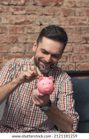 satisfied male entrepreneur saving money in his piggy bank vertical shot. High quality photo