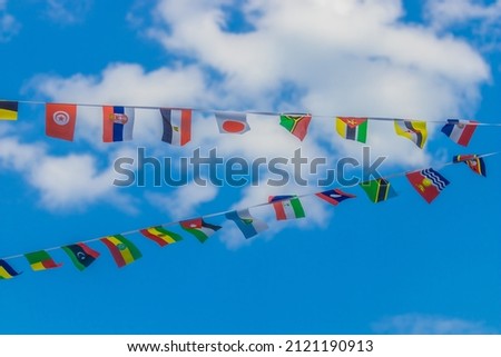 Colorful paper flags of different countries hanging on wires, blue sky in the background. International travel concept.