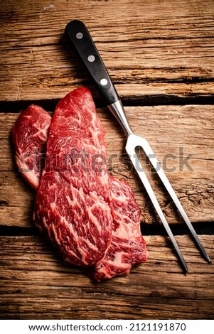 Fresh raw steak with fork. On a wooden background. High quality photo