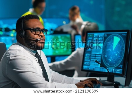 Aircraft flight control officer monitors the approach of aircraft from control tower. Air services office is equipped with navigation systems, radars and computer stations. Aviation concept. Royalty-Free Stock Photo #2121198599