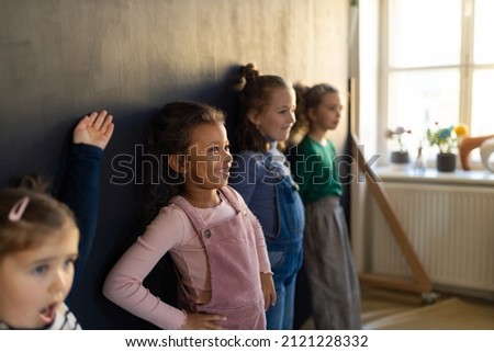 Group of little girls posing in front of blackboard wall paintings indoors in playroom.