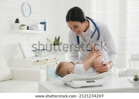 Young pediatrician weighting cute little baby in clinic Royalty-Free Stock Photo #2121234269