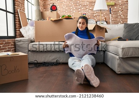 Young hispanic woman looking house plans at new home