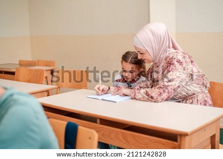 Young teacher in hijab teaching kid students during the class in the classroom at school desk.