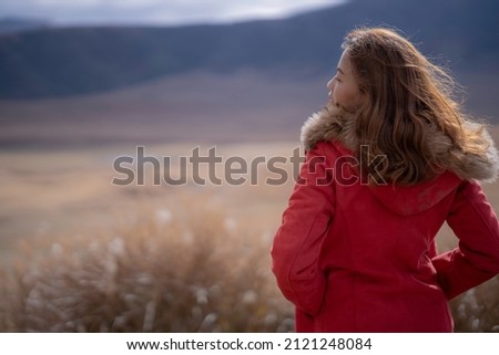 Portrait of woman in red coat and brown fur standing in front of volcano in Japan, tuning back to camera. Travelling moment of girl in beautiful view.