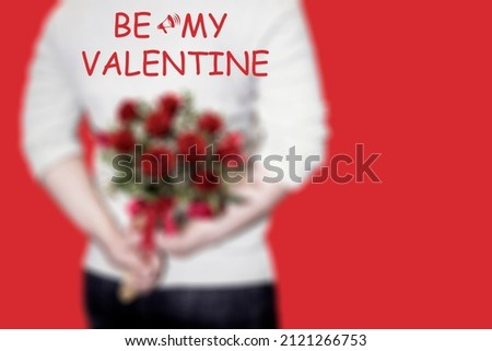 Blurred young Man holding flower bouquet of red roses behind back isolated on red background with text -be my Valentine. Copy space