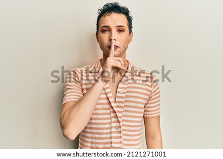 Handsome man wearing make up wearing casual t shirt asking to be quiet with finger on lips. silence and secret concept. 