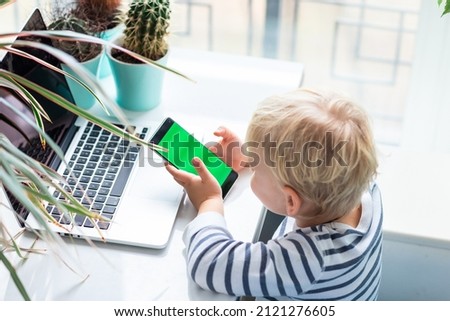 Cute baby boy watching, playing on the phone, focus on chromakey green screen of the mobile phone.