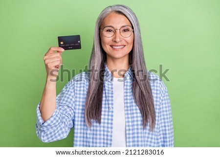 Photo of optimistic elder grey hairdo lady show card wear eyewear plaid shirt isolated on green color background