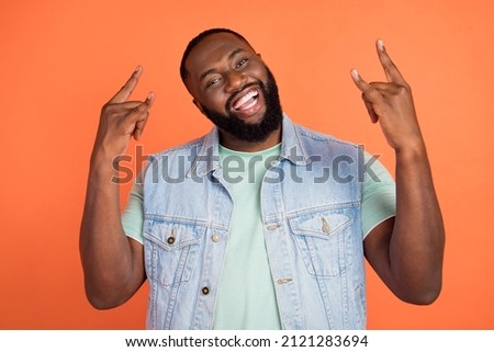Photo of cool funny afro guy wear denim vest showing hard rock sign isolated orange color background