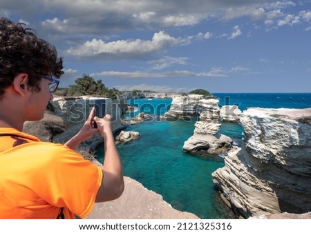 Melendugno, province of Lecce, Puglia, Italy. August 2021. The stacks of Sant'Andrea are an amazing naturalistic attraction: a young man takes pictures with his smartphone.
