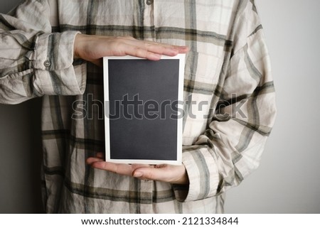 The girl is holding a book with a black cover and a white frame. Place for text and advertising. Book or stylish notebook close-up