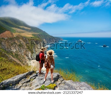 Couple on hiking trip resting on top of the mountain looking at ocean view. People enjoying beautiful coastal scenery. Pacific Ocean, Big Sur, California, USA Royalty-Free Stock Photo #2121337247