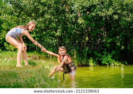 Blond preteen sister helps little brother out of the water. Summer, holiday, outdoor activities at summer time concept.