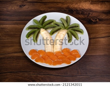 palm tree with fruit on a white plate - a picture of kiwi fruit, banana, tangerine. Food for vegetarians, dietary fruit composition