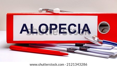 On the desktop is a stethoscope, documents, a pen, and a red file folder with the text ALOPECIA. Medical concept