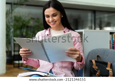 Young woman reading book at table in library and smiling toothy. Brunette lady studying at the high school. Stock photo 