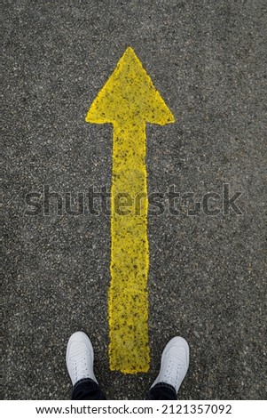 Person with white sneaker and yellow arrow on the street, space for text