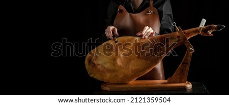 Professional cutter carving slices from a whole bone-in serrano ham, Spanish jamon iberico, Jamon Serrano, Bellota, Italian Prosciutto Crudo or Parma ham, Royalty-Free Stock Photo #2121359504