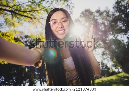 Photo of sweet shiny young lady wear checkered shirt glasses smiling showing v-sign tacking selfie outdoors urban city park