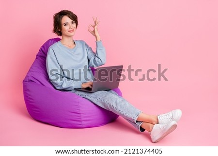 Full size photo of funny millennial lady sit work latop show okey wear sweatshirt jeans sneakers isolated on pink background