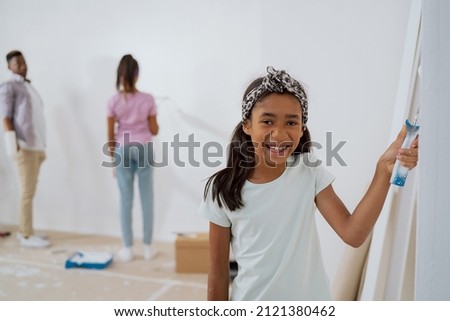 Portrait of a girl helping a family to painting walls in a room, the child is having fun in the renovation of the apartment, learning to use a paint roller