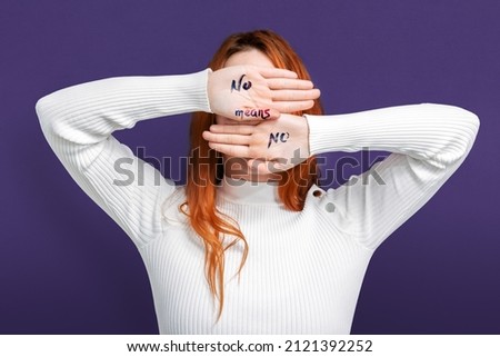 Girl covering her face with her hands written with no means no on purple background color feminism