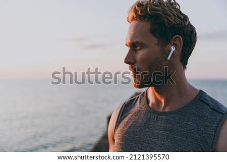 Close up side view young strong athletic toned fit sportsman man in sports clothes earphones warm up train with music at sunrise sun dawn over sea beach outdoor on pier seaside in summer day morning. Royalty-Free Stock Photo #2121395570