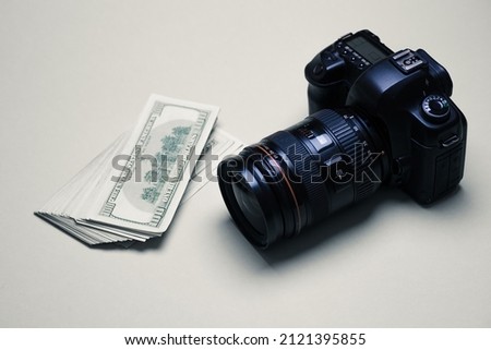 A stack of cash dollars next to a professional photo camera. The concept of earnings, the development of a photographer, the work of paparazzi, expensive photographic equipment. Copy space.